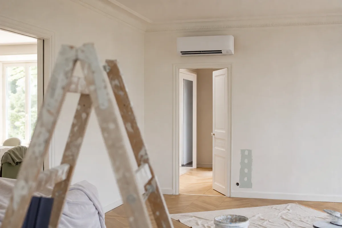 Unité intérieure murale de climatisation réversible posée au-dessus d’une porte dans un séjour en rénovation